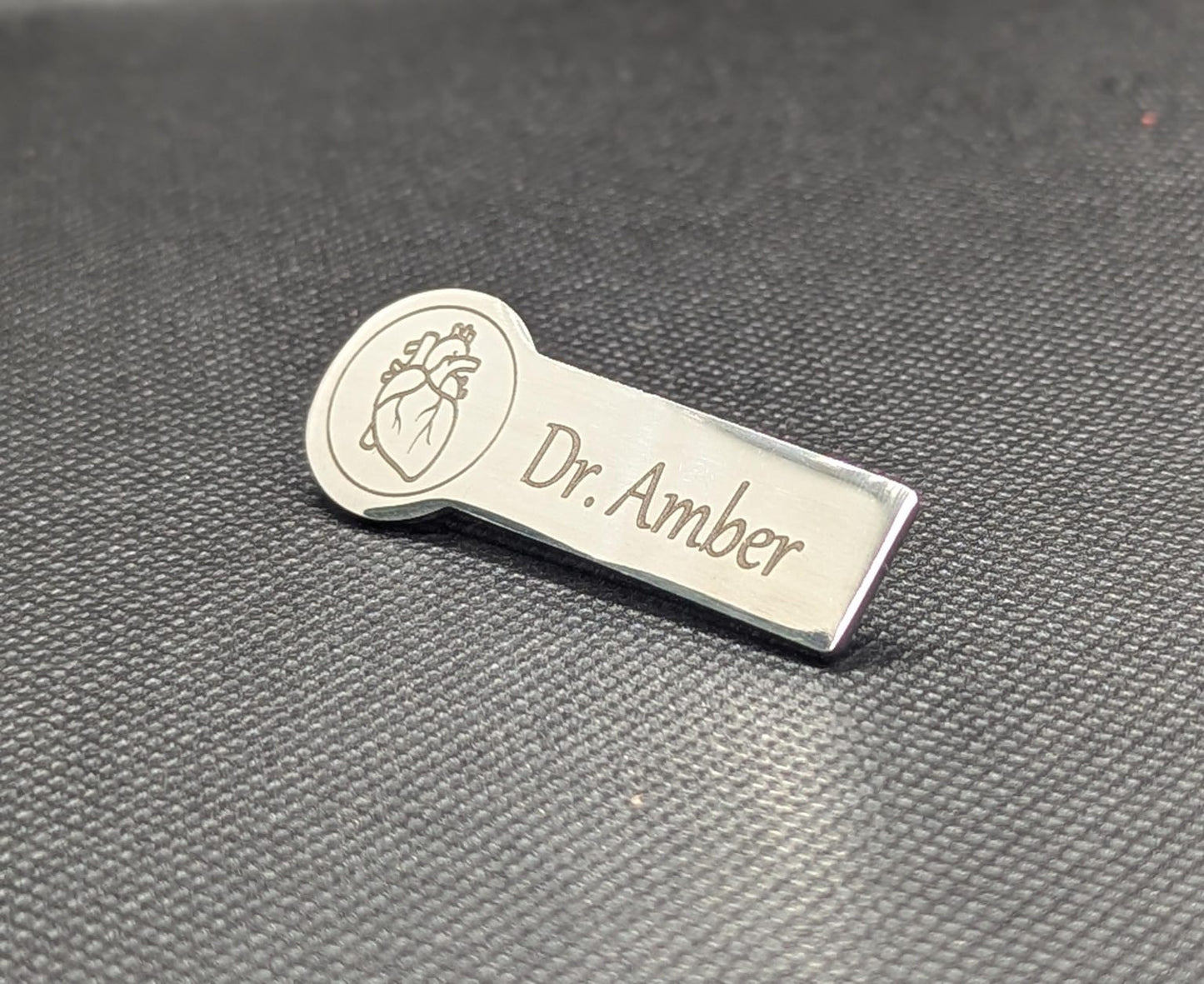 Metallic name tag with name and heart design on a textured gray background
